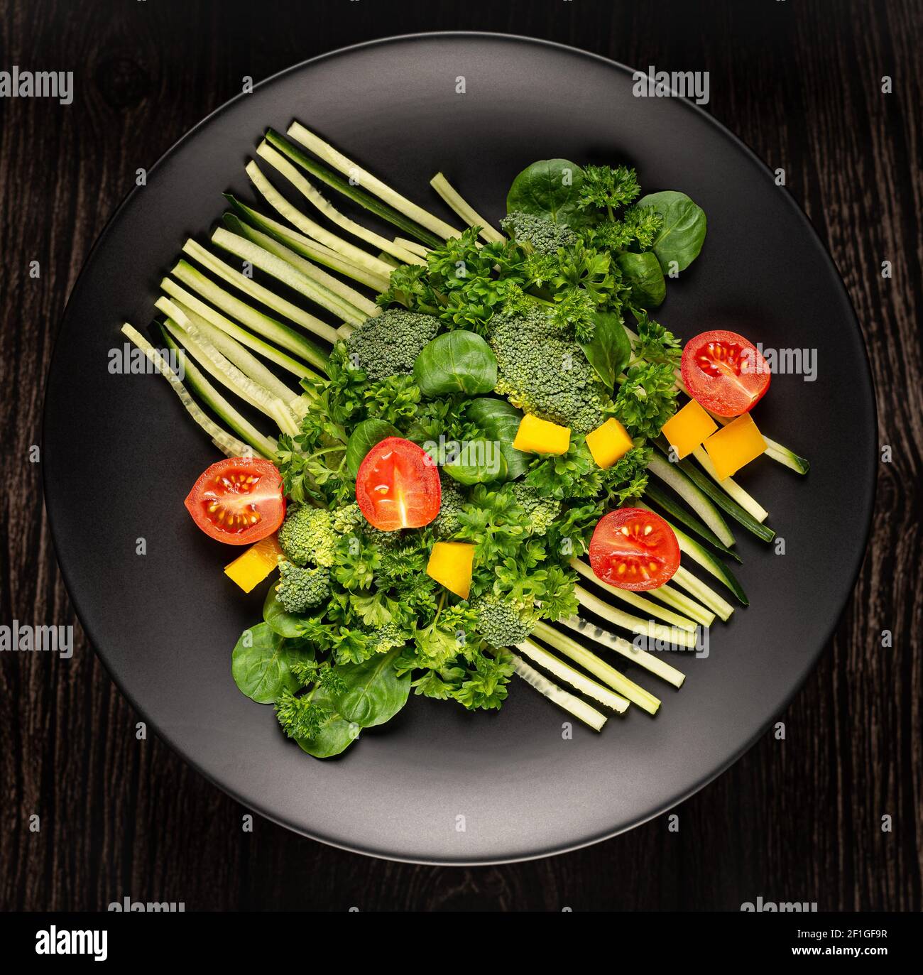 Les légumes en tranches sont sur une assiette noire sur un fond noir photographié. Vue de dessus. Banque D'Images