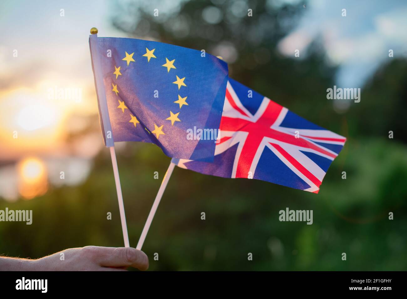 Les drapeaux du Royaume-Uni et de l'Union européenne sont tenus à la main contre le coucher de soleil d'un beau paysage en été. Banque D'Images