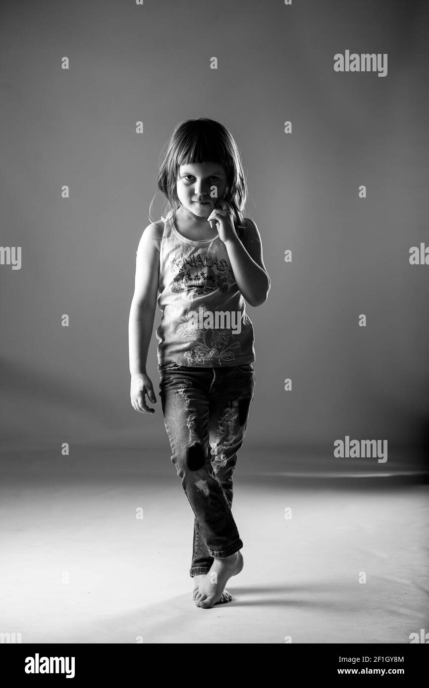 Petite fille blonde souriante avec robe rose sur fond gris et noir et blanc séance photo en studio. Banque D'Images