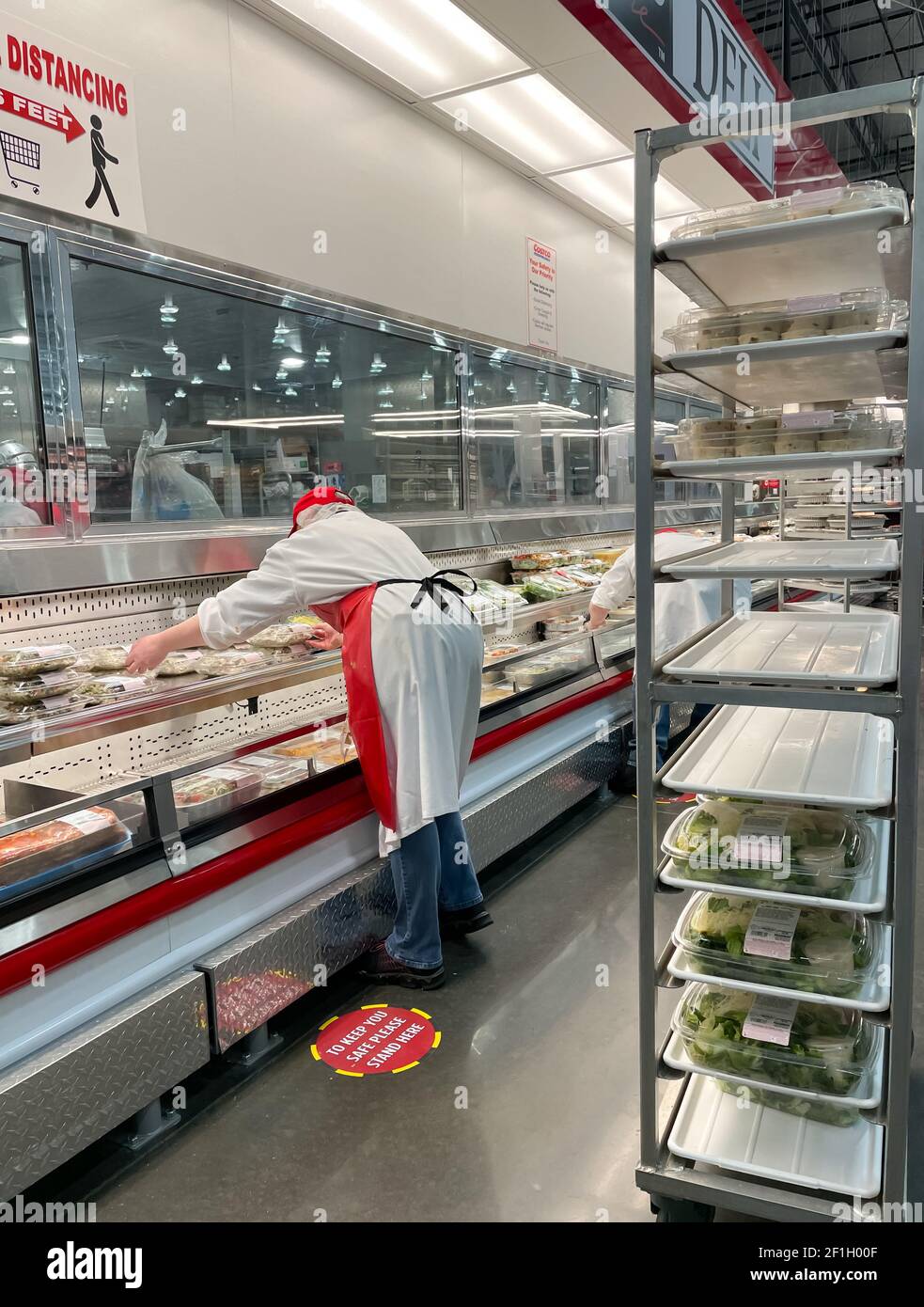 McKinney, TX USA - 22 février 2021 : employé de Costco deli rechaussant les plateaux à salade sur l'étagère Banque D'Images