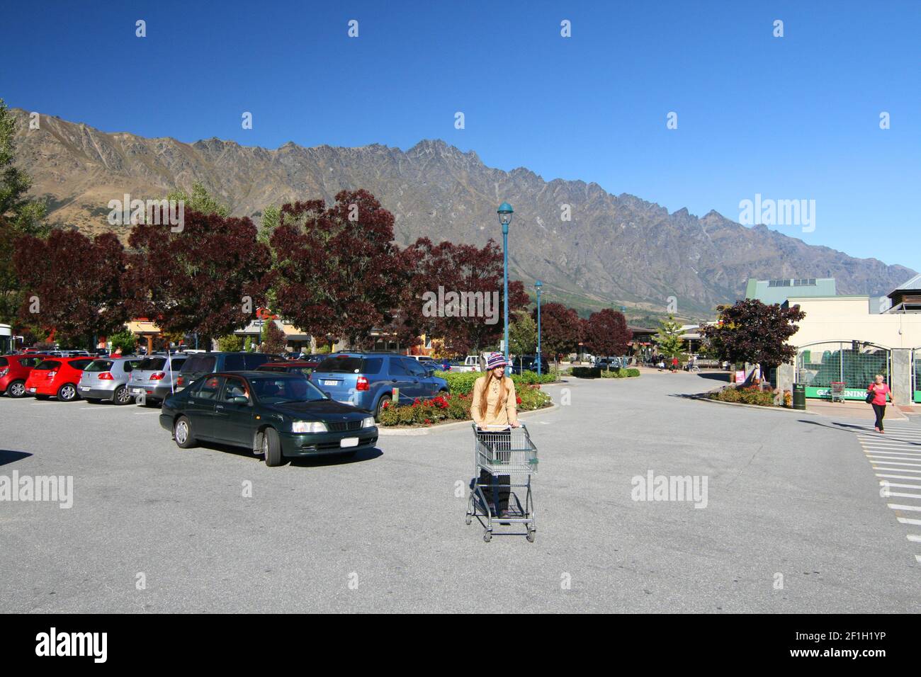 Femme avec un chariot à provisions au centre commercial de Remarkables Park, Frankton, Queenstown, vue sur les montagnes de Remarkables derrière, Nouvelle-Zélande Banque D'Images