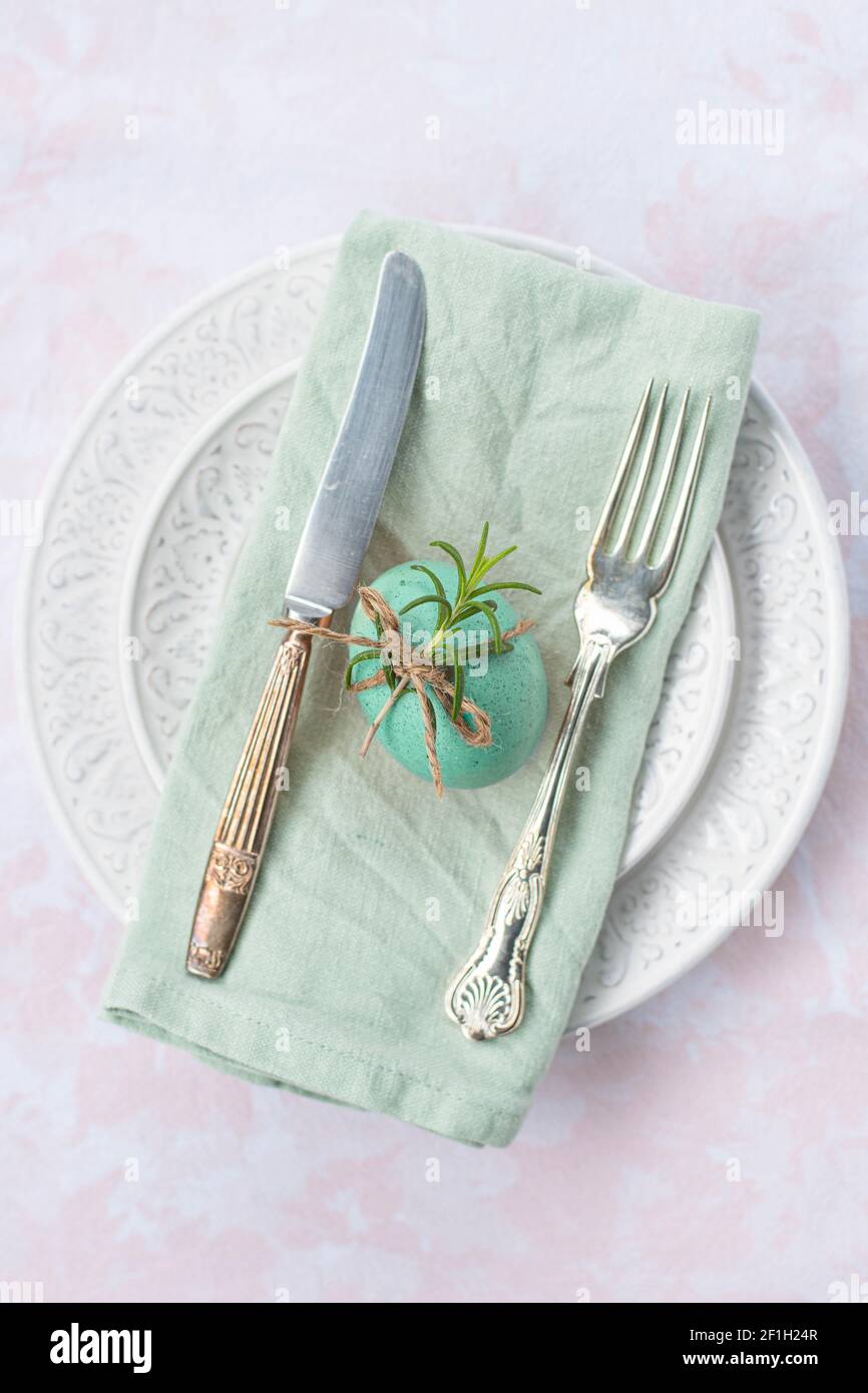 Oeuf de Pâques coloré décoré avec une corde rustique et un vert tige posée sur une assiette avec des couverts vintage Banque D'Images