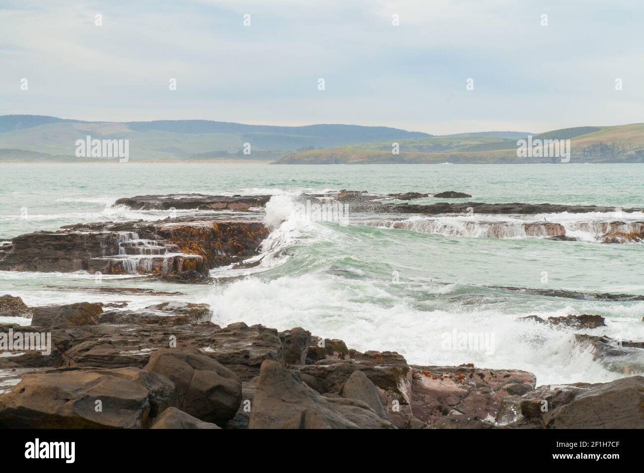 Des vagues sauvages de l'océan Pacifique s'écrasont sur des rochers à l'entrée de la baie de Porpoise, côte rugueuse du sud, Nouvelle-Zélande Banque D'Images