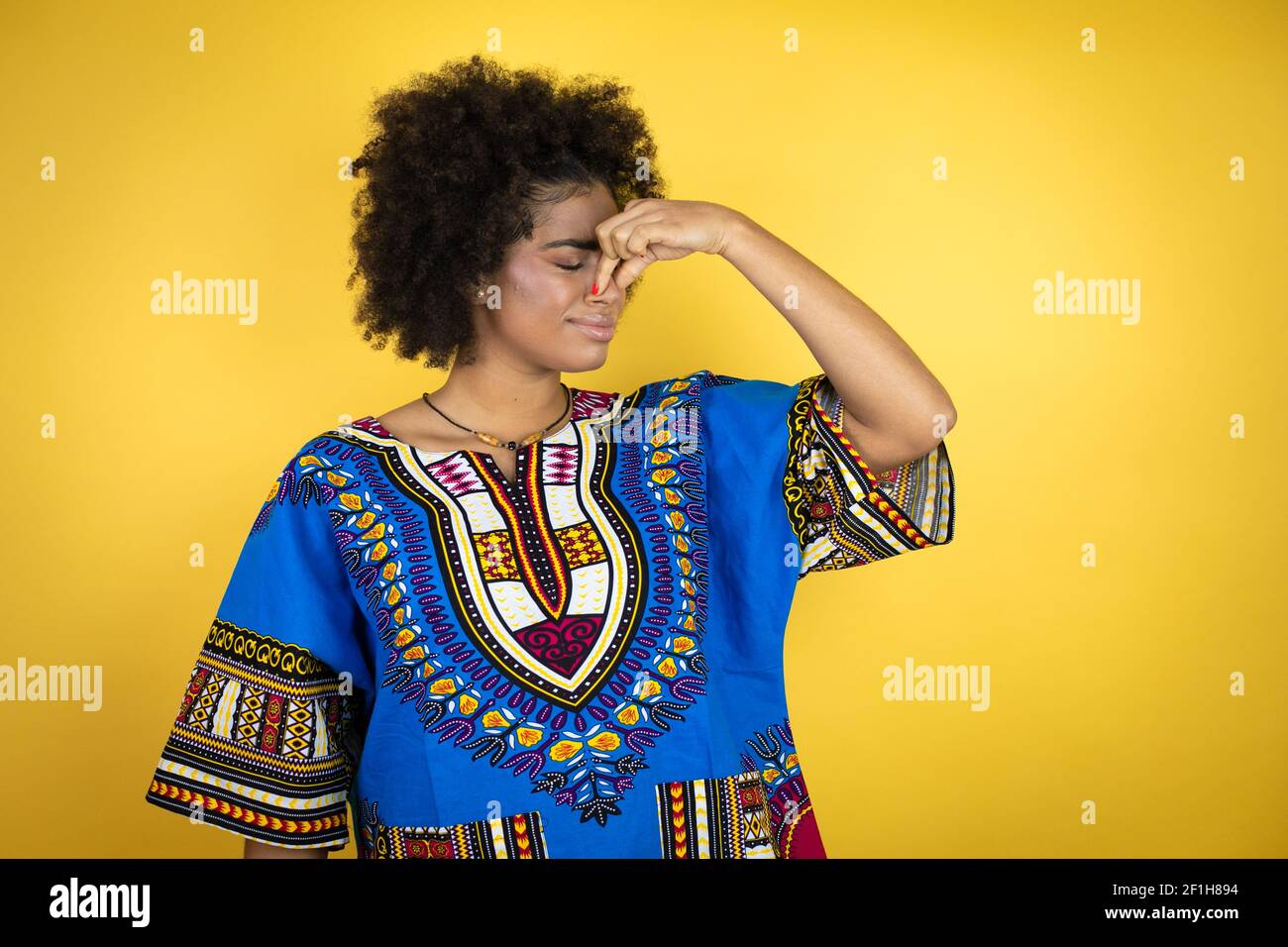 Femme afro-américaine portant des vêtements africains sur fond jaune,  sentant quelque chose de stinky et dégoûtant, une odeur intolérable, tenant  le souffle avec humour Photo Stock - Alamy