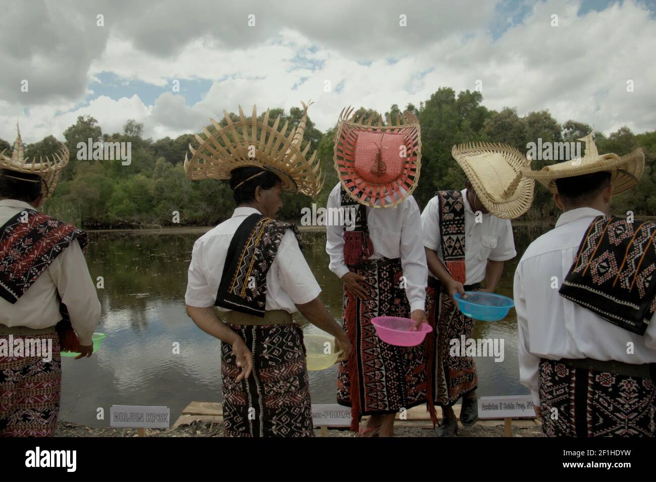 Les hommes portant des vêtements traditionnels tenant des bols en plastique lors de la préparation d'un événement cérémonial pour libérer les tortues endémiques à col serpent (Chelodina mccordi) se sont élevés en captivité à son habitat convenable dans le lac Peto, l'île de Rote, à l'est de Nusa Tenggara, en Indonésie. Banque D'Images