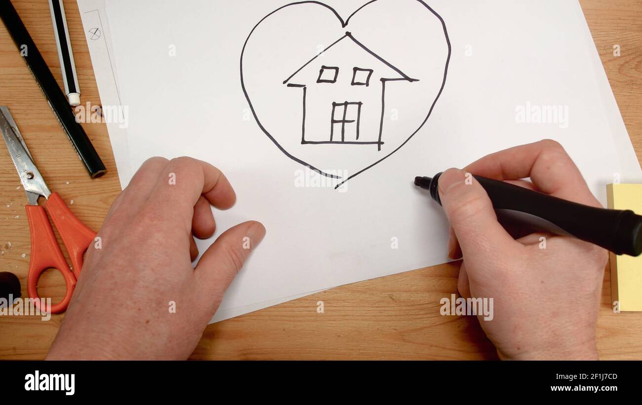 Vue de dessus, la main d'un architecte d'intérieur dessine une maison à l'intérieur d'un coeur sur une feuille de papier, pied idéal Banque D'Images