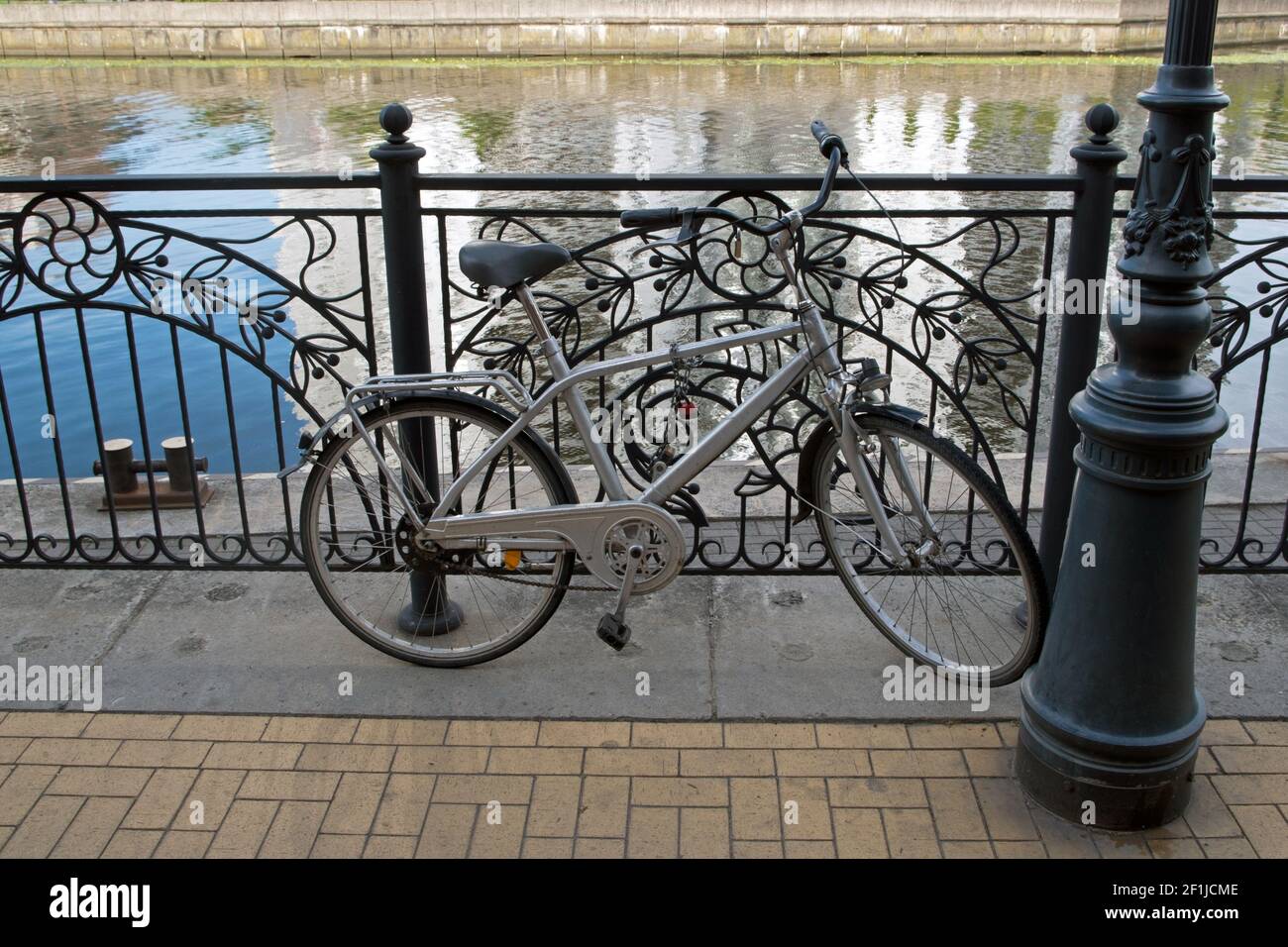 Une bicyclette grise est garée près d'un lampadaire et enchaînée à la main courante en métal noir d'une rivière carrelée de jaune remblai avec reflets scintillants Banque D'Images