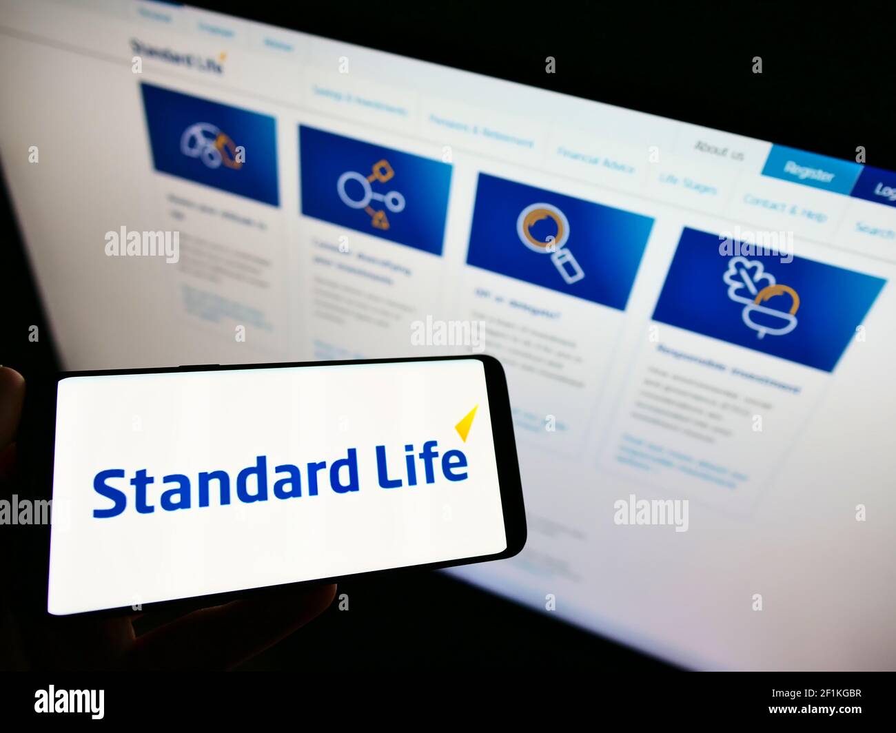 Personne tenant un téléphone portable avec le logo d'entreprise de la marque britannique d'assurance Standard Life à l'écran en face de la page Web. Mise au point sur l'affichage du téléphone. Banque D'Images