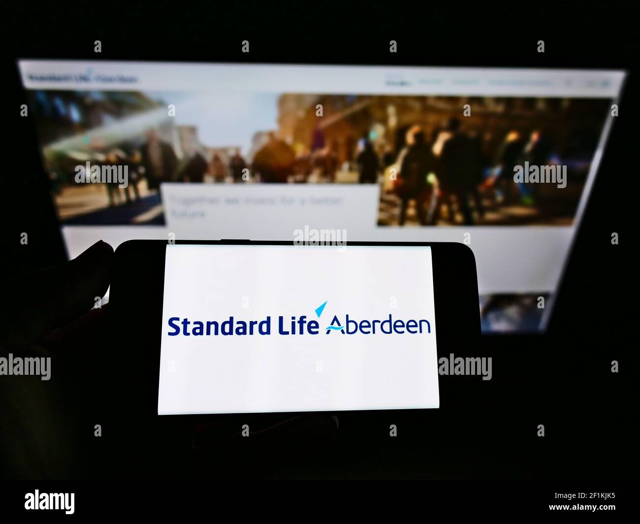 Personne tenant un téléphone portable avec le logo de la société d'investissement britannique Standard Life Aberdeen à l'écran en face de la page Web. Mise au point sur l'affichage du téléphone. Banque D'Images