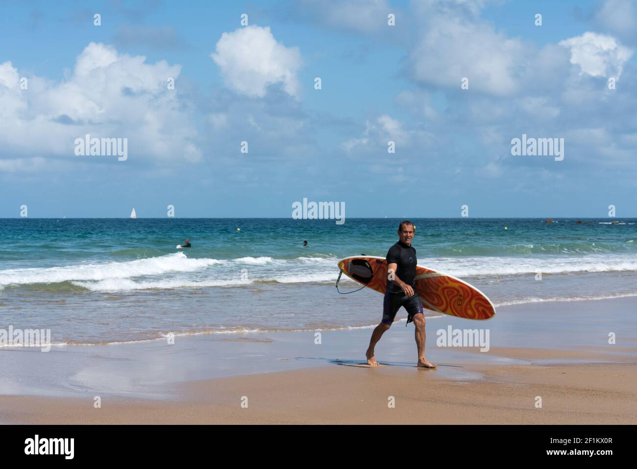 Surfeur d'âge moyen marchant sur la plage après un surf amusant Session dans les vagues sur la côte de BRI Banque D'Images