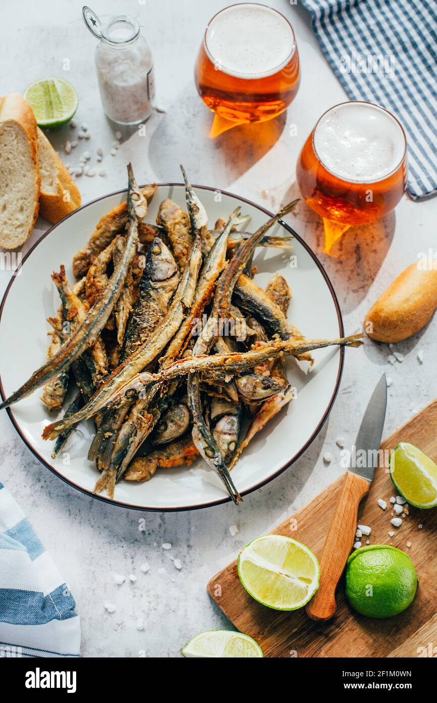 gros plan de l'anchois frit dans une assiette à côté bière en verre et citron vert sur une planche Banque D'Images