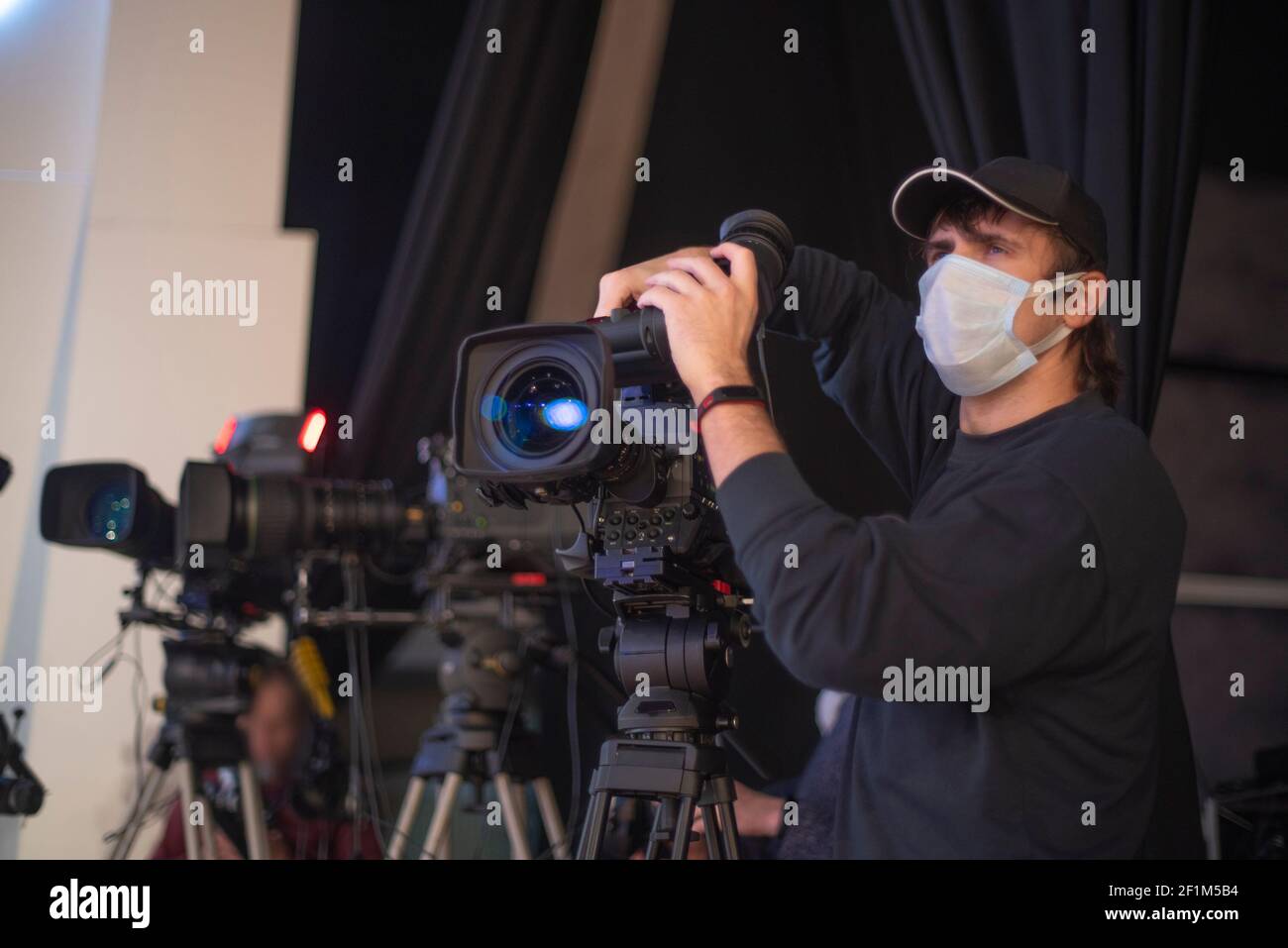 un caméraman masqué filme un spectacle télévisuel en studio. TÉLÉVISION Banque D'Images