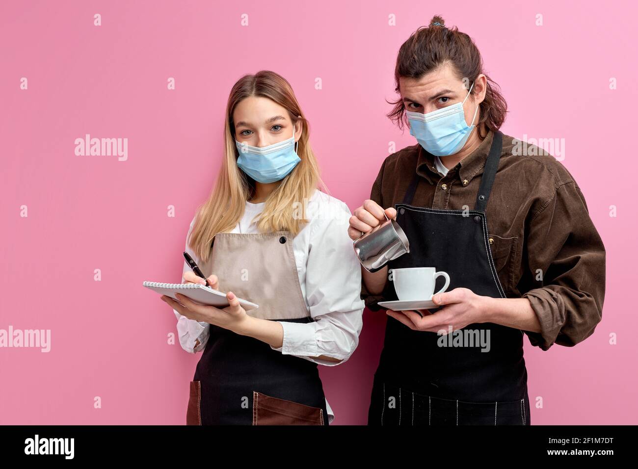 Les jeunes serveurs prêts à servir les clients dans un café ou un restaurant, se posent à la caméra isolée sur fond rose, le serveur mâle versant le café dans le blanc Banque D'Images