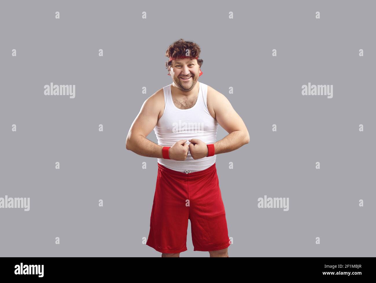 Joyeux homme en débardeur et short souriant et flexible ses bras montrant ses muscles Banque D'Images