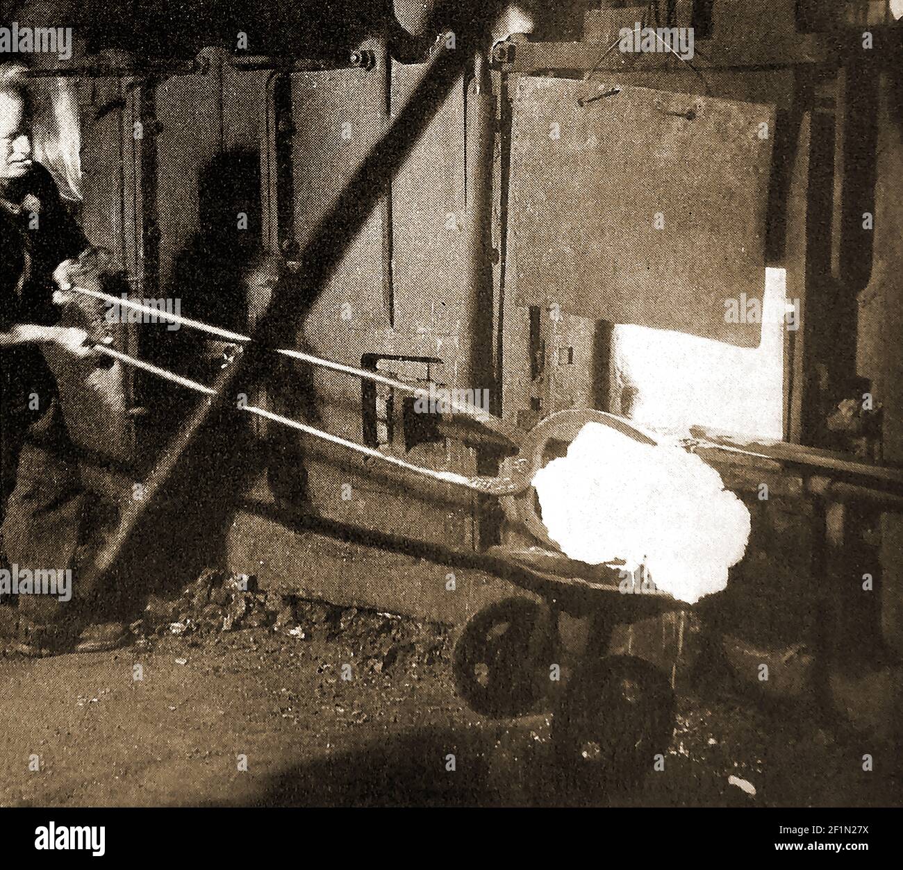 Image des années 1930 d'un homme qui puise de la fonte dans une fonderie de fer britannique et extrait la boule pudled du four. Le processus de puddling est une étape dans la fabrication de fer de haute qualité à l'aide d'un creuset ou d'un four, inventé en Grande-Bretagne pendant la Révolution industrielle. Le fer à barres pourrait être produit sans charbon de bois et a remplacé les procédés d'enrobage et d'estampage, d'utilisation du charbon de bois et de bloomerie précédents. Banque D'Images