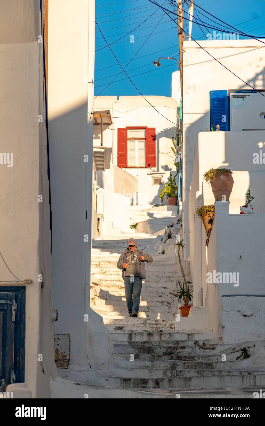 Un homme marche sur les marches à blanc lavé rues étroites avec fenêtres et portes par temps ensoleillé Avec ciel bleu dans une île grecque Banque D'Images