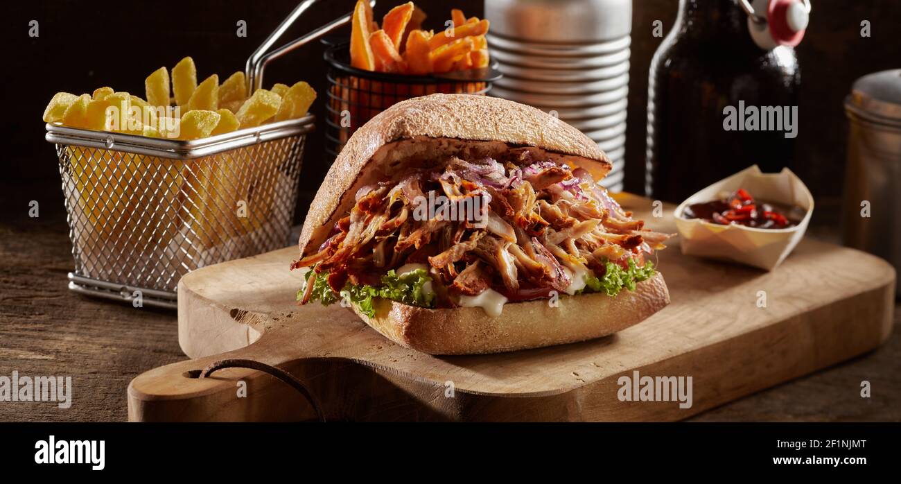 Savoureux hamburger de porc et frites servis sur bois table avec sauce sur fond noir Banque D'Images