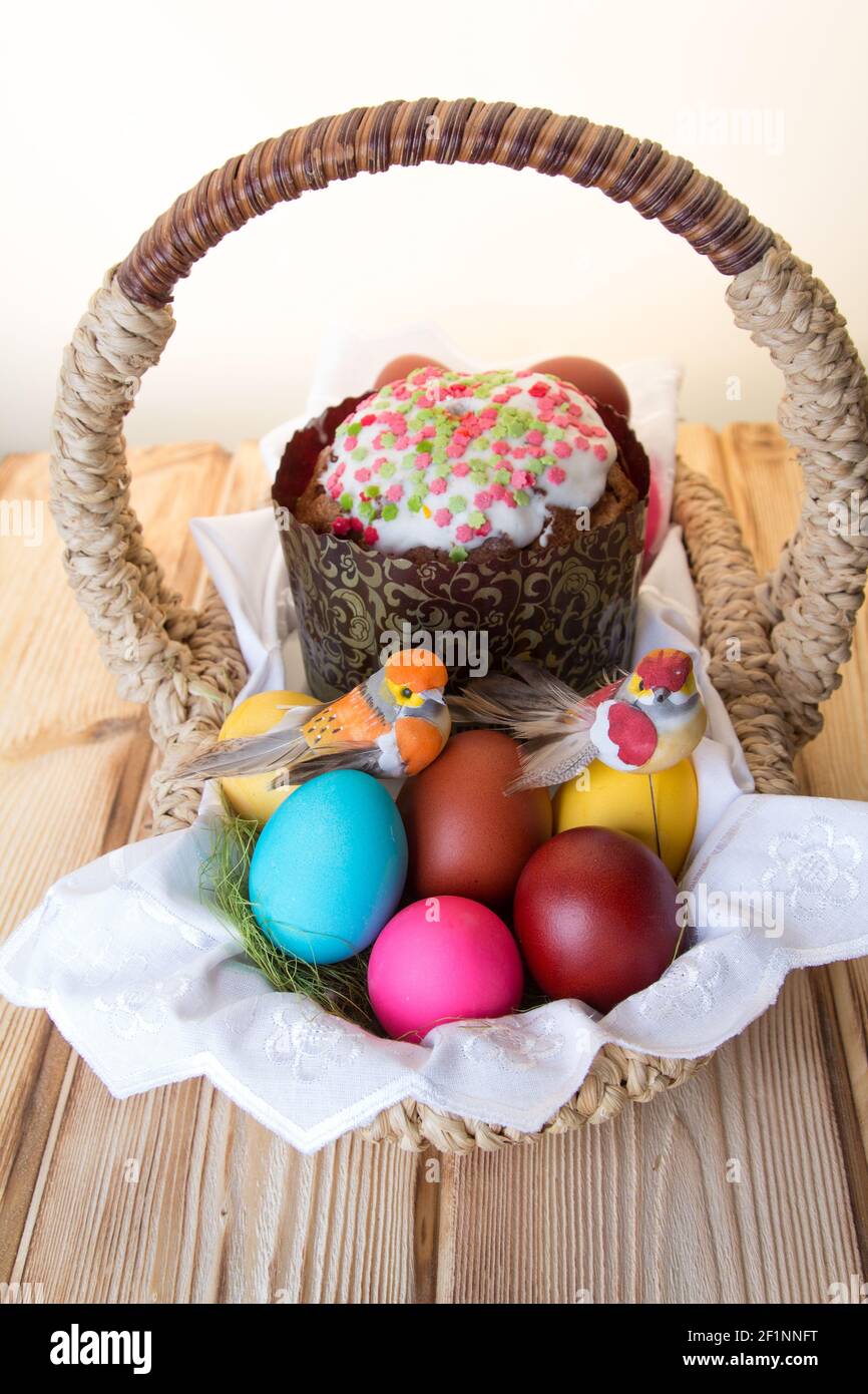 Un panier de Pâques avec un oiseau jouet assis sur des œufs de couleur vive et un gâteau . Banque D'Images