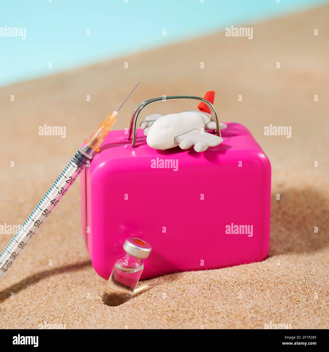 un flacon, une seringue, une valise rose et un avion sur le sable, sur fond bleu, représentant le tourisme médical Banque D'Images