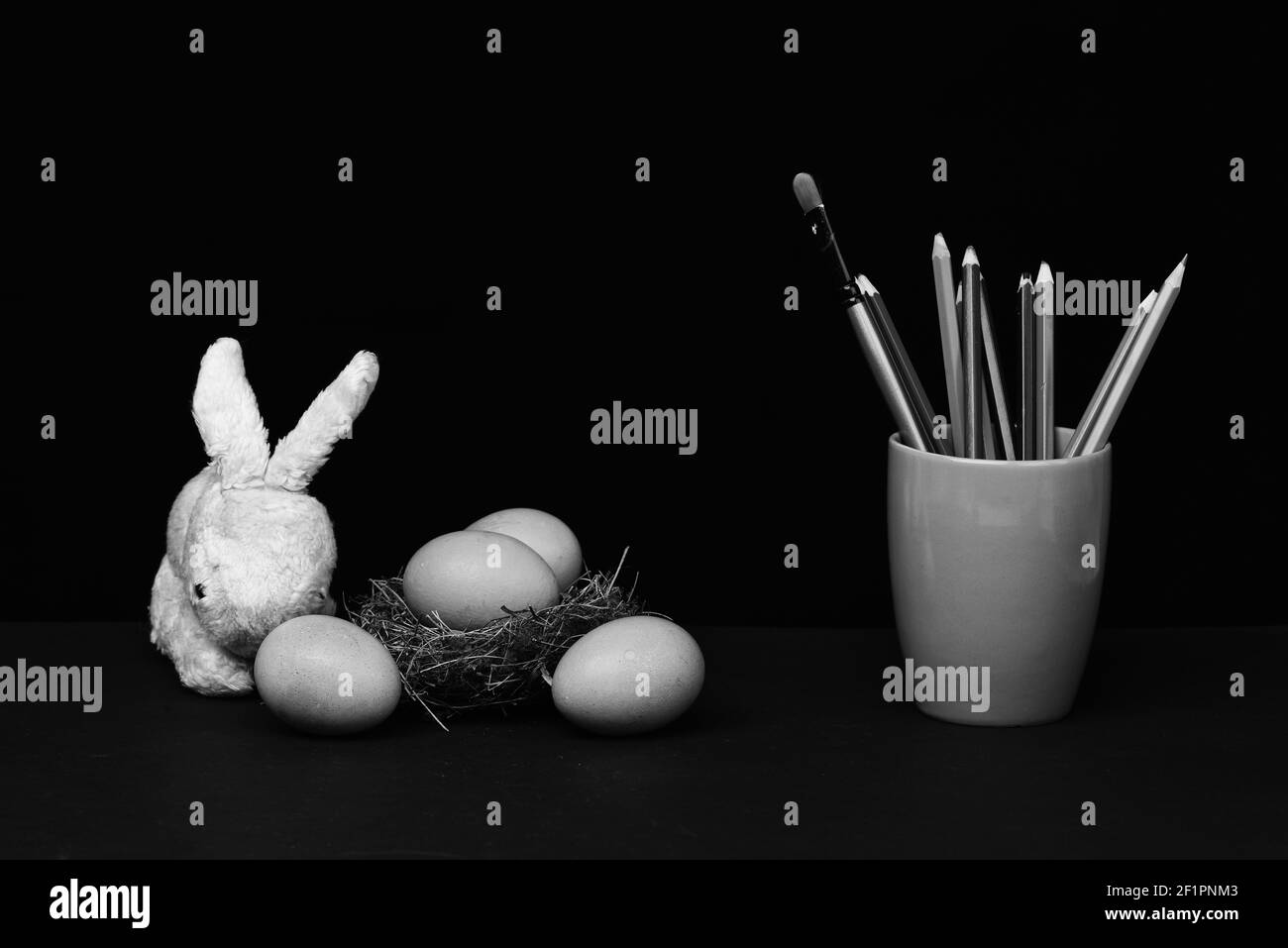 ensemble d'œufs traditionnels peints en bleu dans le nid et une tasse avec des crayons et pinceau avec jouet de lapin isolé sur fond noir. Concept joyeuses Pâques, espace copie Banque D'Images