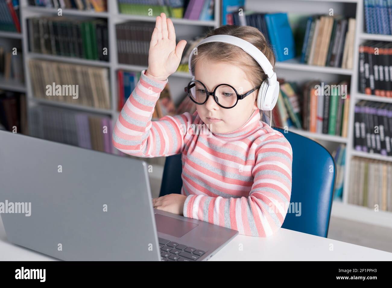 Fille d'école étudie en ligne. Enseignement à domicile. Enseignement à distance. La fille lève sa main pour répondre à l'enseignant. Photo de haute qualité Banque D'Images