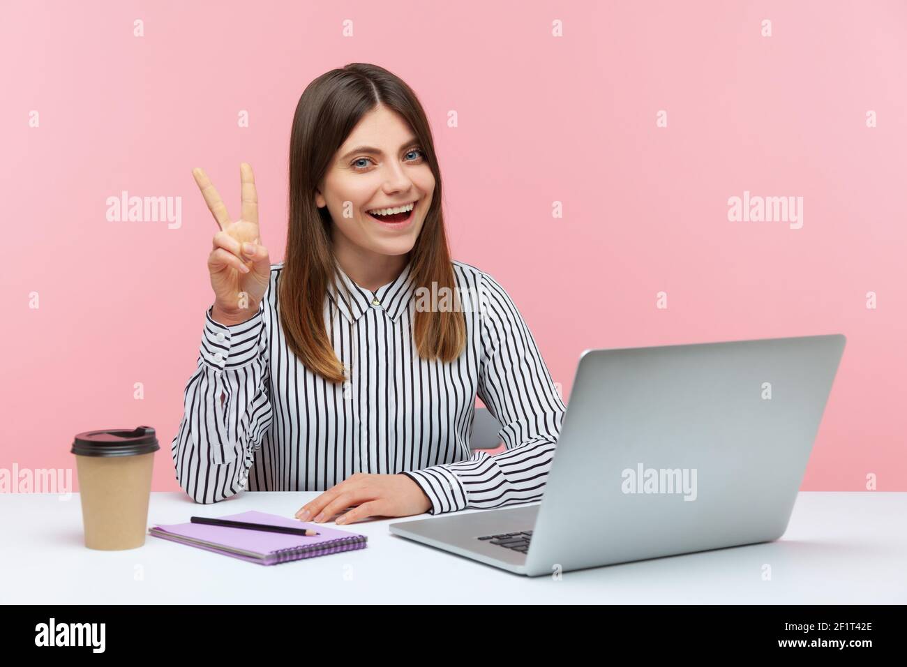 Une femme d'affaires gaie excitée montrant le geste de la victoire, célébrant le projet réussi, faisant signe v au bureau à domicile de lieu de travail. Salle de studi Banque D'Images