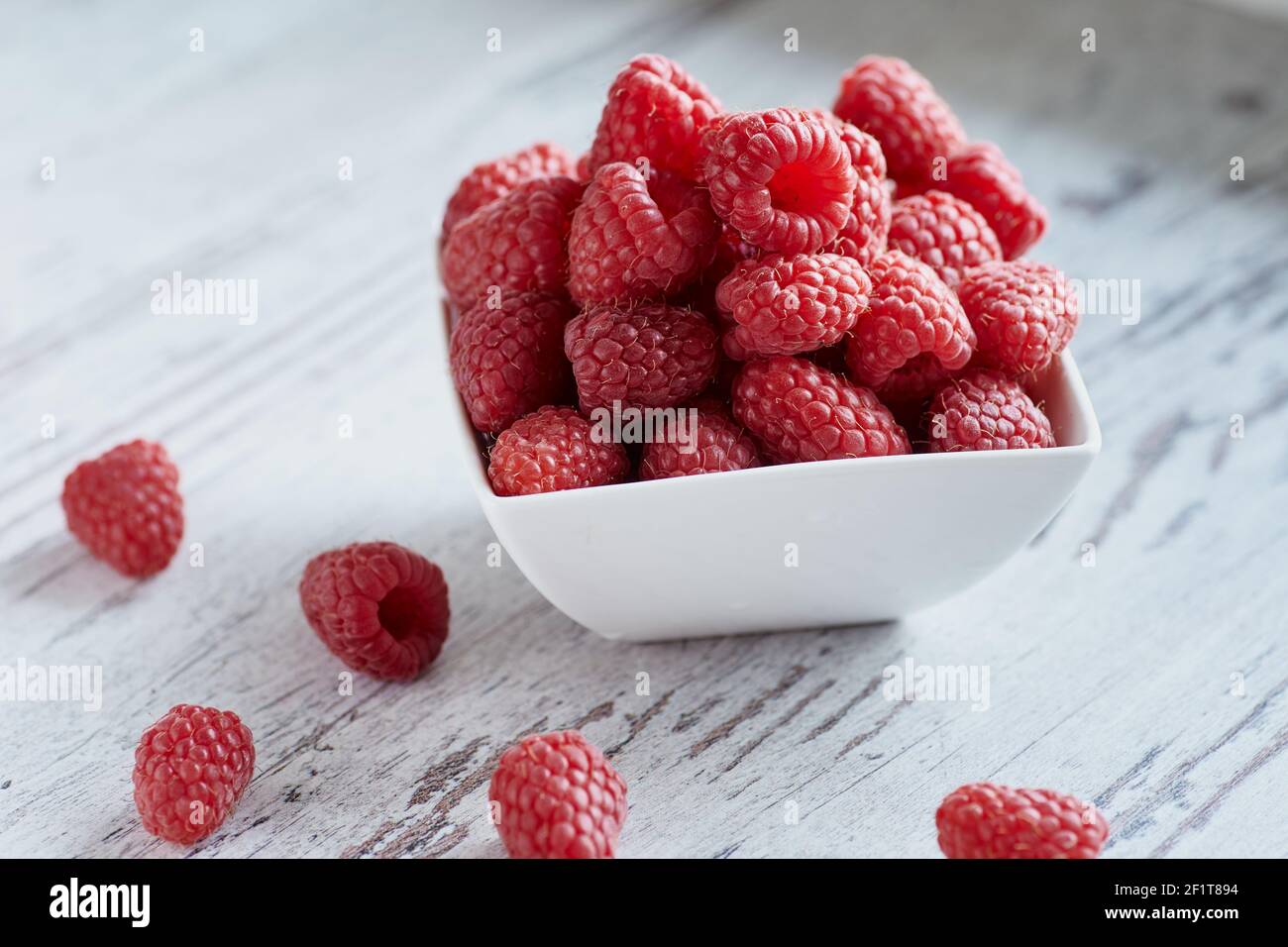 Photo en gros plan des framboises dans un bol blanc sur une table en bois blanc. Banque D'Images