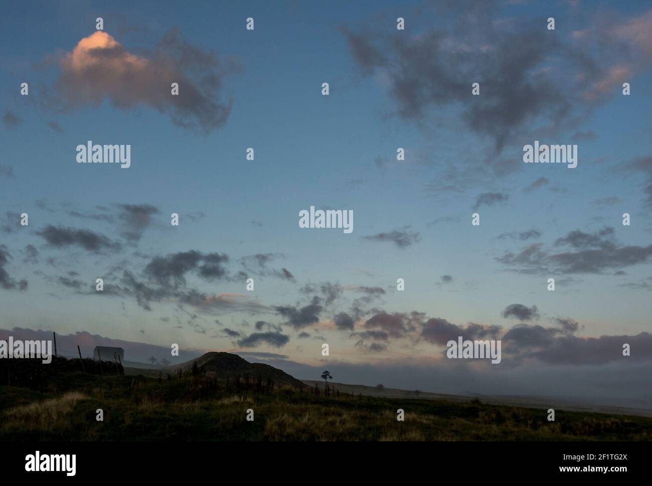 Une bosse verte, gâtez d'une ancienne mine, vue à côté d'une grange noire contre le soleil, nuages en soirée en automne dans les Pennines du Nord Banque D'Images