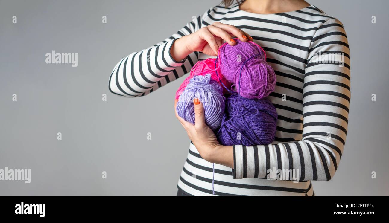 Femme avec t-shirt rayé et vernis à ongles orange tenant certains boules de laine violet et rose avec espace de copie Banque D'Images