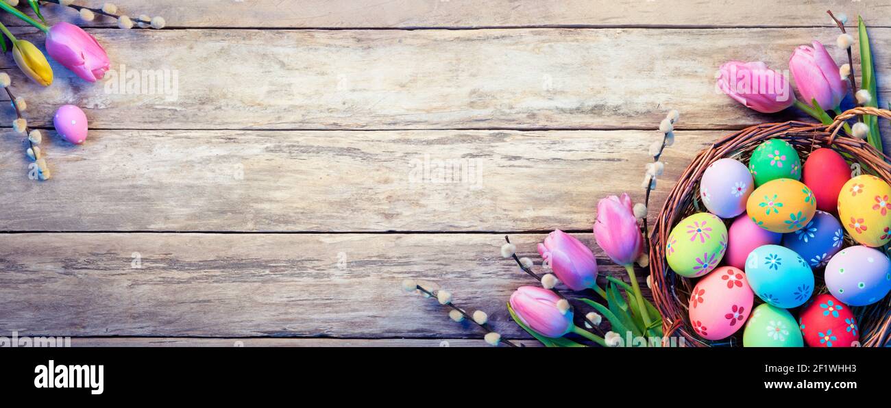 Décoration de Pâques - oeufs peints dans le panier avec tulipes Planche en bois naturel Banque D'Images