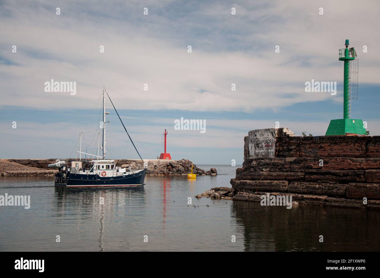 Un bateau part vers la mer, passant entre les feux de navigation rouges et verts qui marquent l'ouverture du port de Santa Rosalia, Baja, Mexique. Banque D'Images