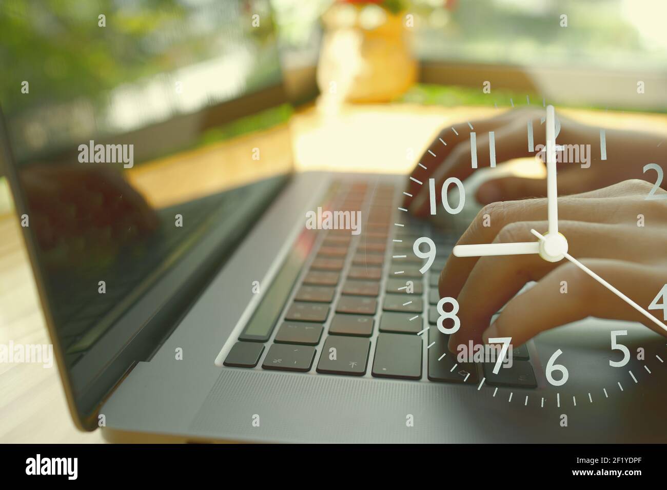 Un résumé dactylographiant à la main un ordinateur portable et une horloge analogique indiquant l'heure de début du lieu de travail. Banque D'Images