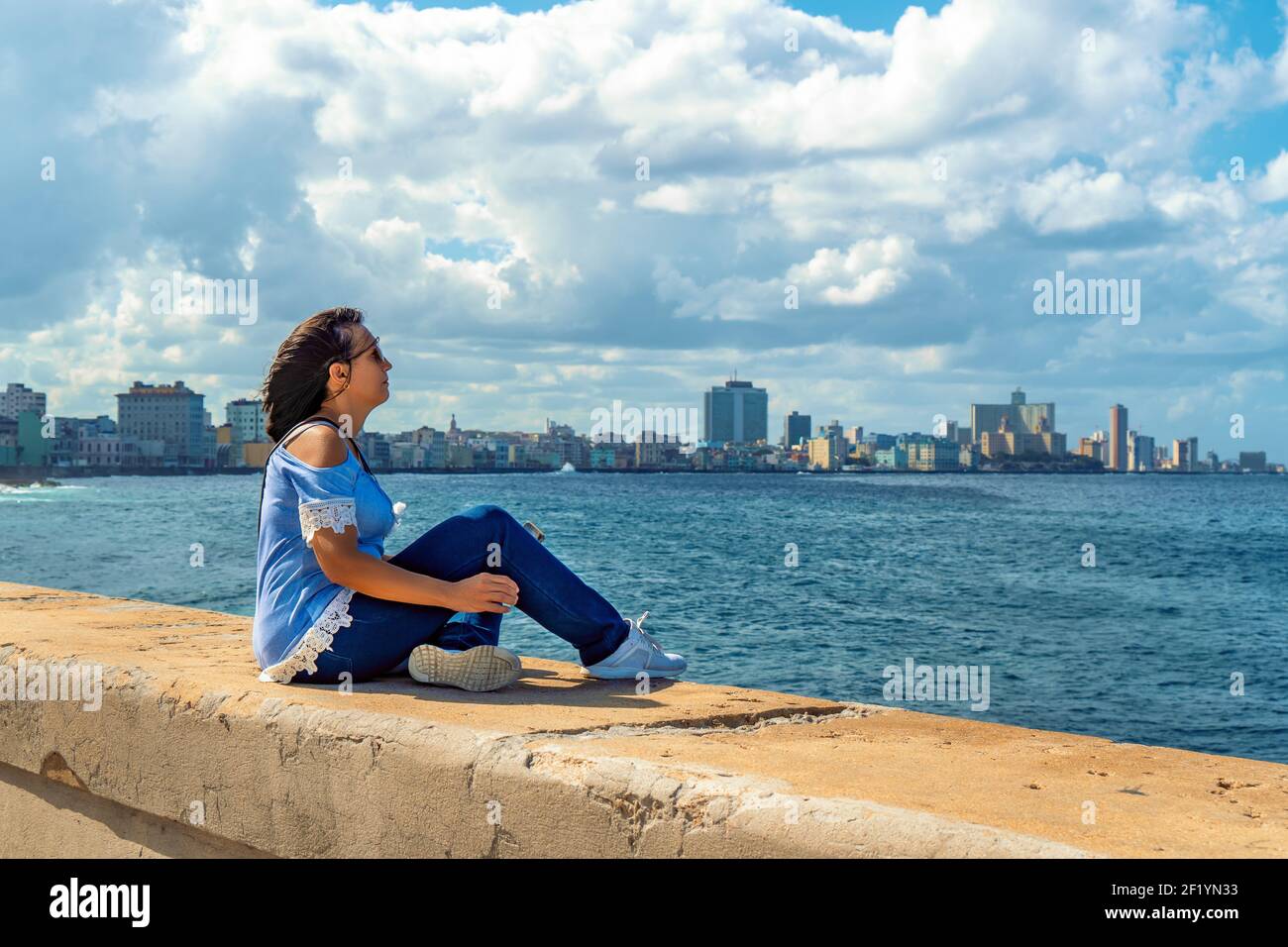 Femme assise sur le Malecon à la Havane en face de la mer. Banque D'Images