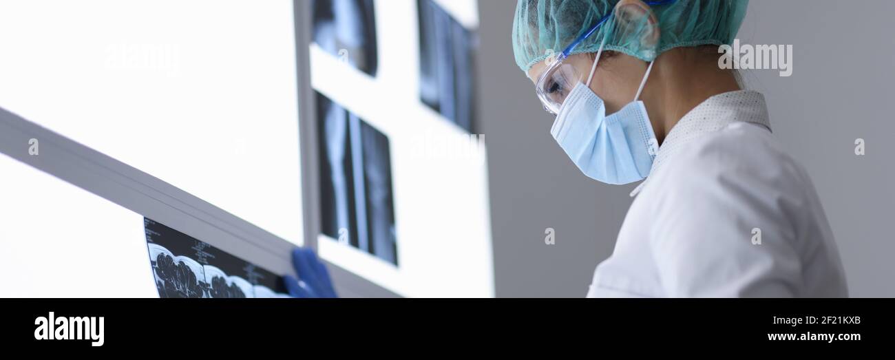 Le médecin en cabinet dans le masque médical de protection et les lunettes regarde l'image de rayons X. Banque D'Images