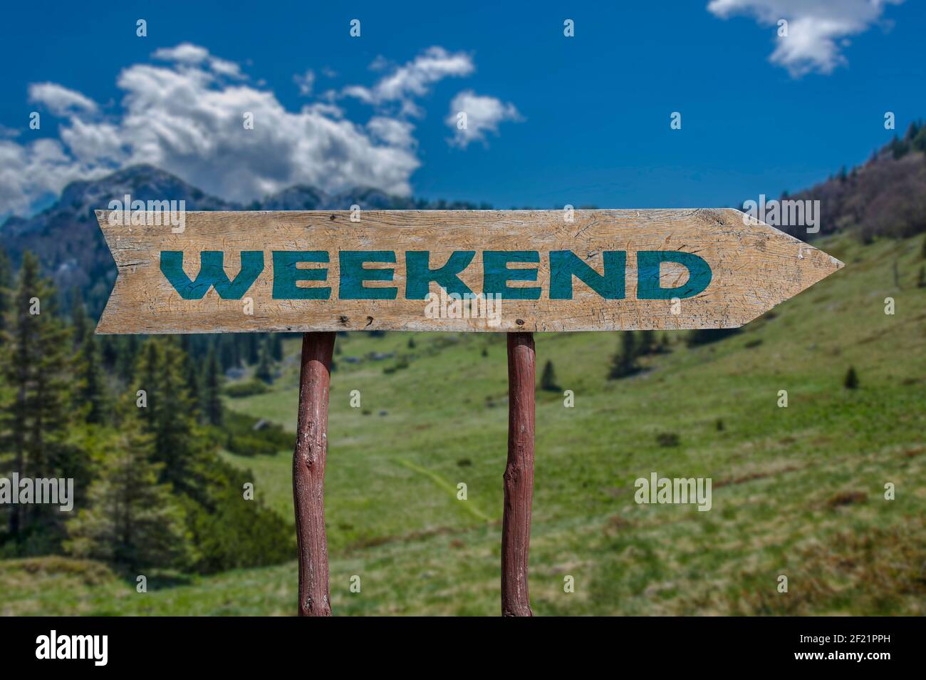 Week-end flèche route en bois panneau contre le soleil été montagnes fond. Banque D'Images