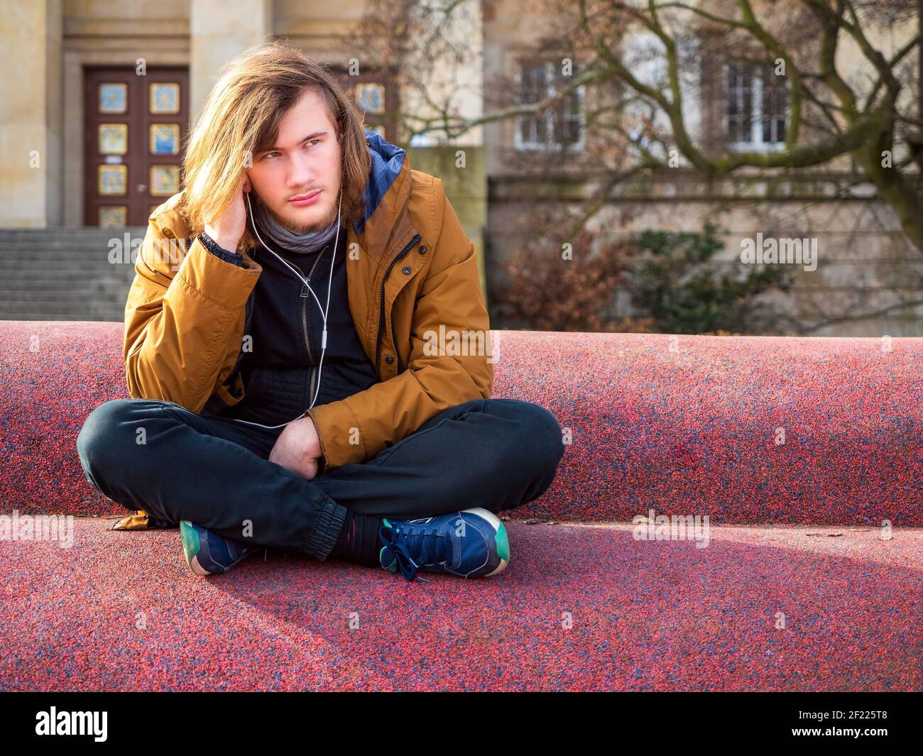 Triste jeune homme assis seul dans une ville en milieu urbain libérez de l'espace et écoutez de la musique Banque D'Images