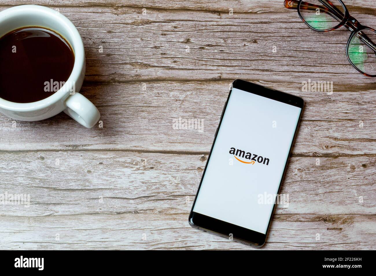 Un téléphone portable ou un téléphone portable posé sur une table Ou un bureau avec l'application Amazon Shopping ouverte et un café à côté Banque D'Images