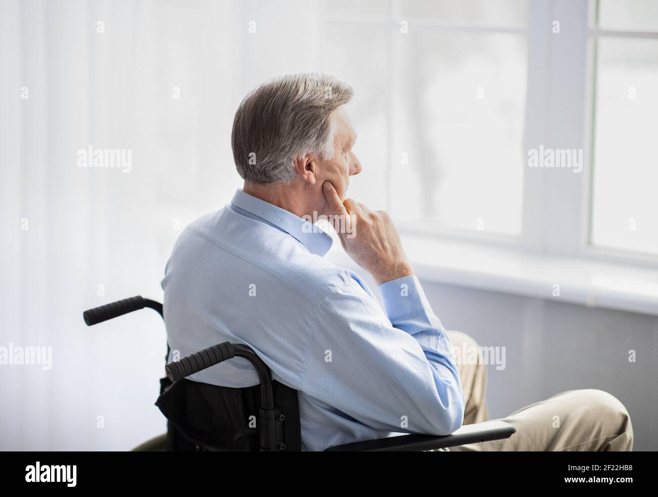 Dépression chez les personnes âgées handicapées. Homme âgé en fauteuil roulant se fermant du monde, regardant par la fenêtre à la maison Banque D'Images