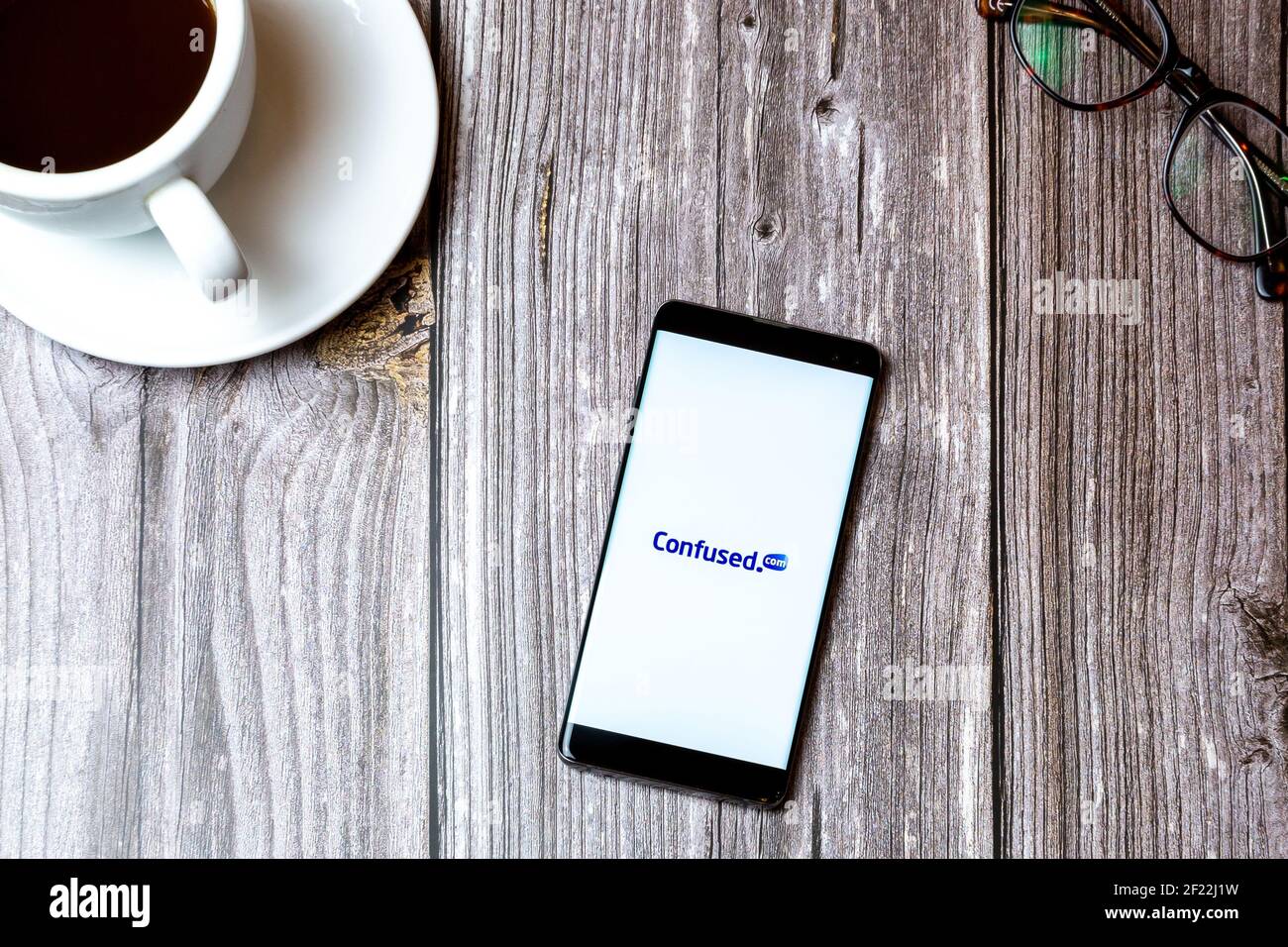 Un téléphone portable ou mobile posé sur un bois Tableau avec l'application Confused.com ouverte à l'écran en regard de un café Banque D'Images