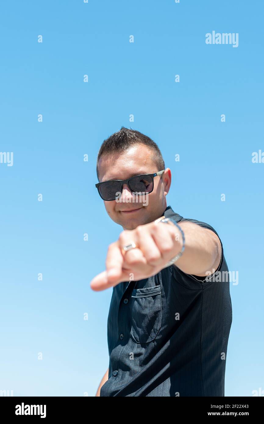 Homme heureux pointant les doigts vers l'appareil photo sur fond de ciel. Banque D'Images