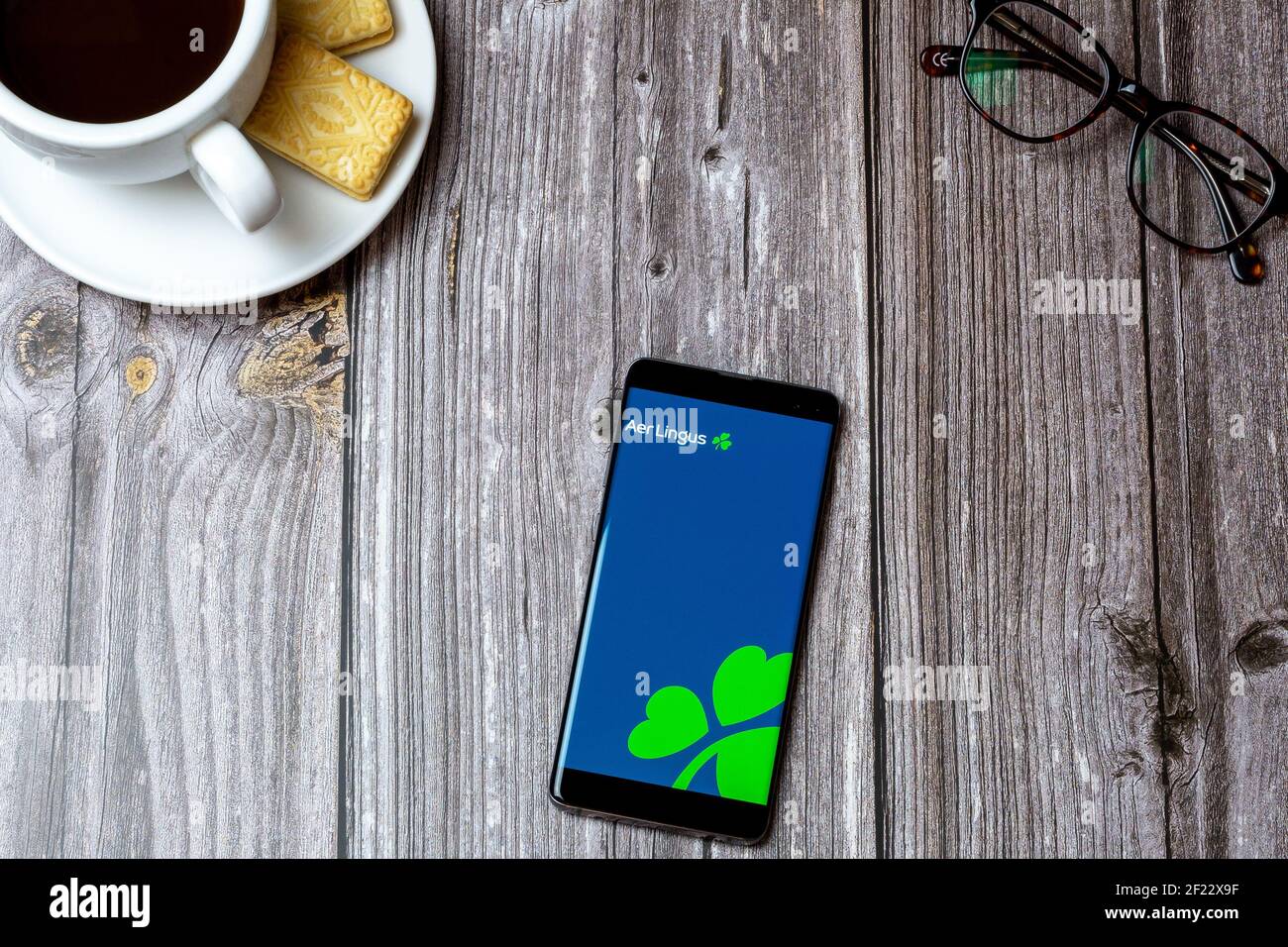 Un téléphone portable ou un téléphone portable sur une table en bois Avec l'application Aer Lingus ouverte à côté d'un café et lunettes Banque D'Images