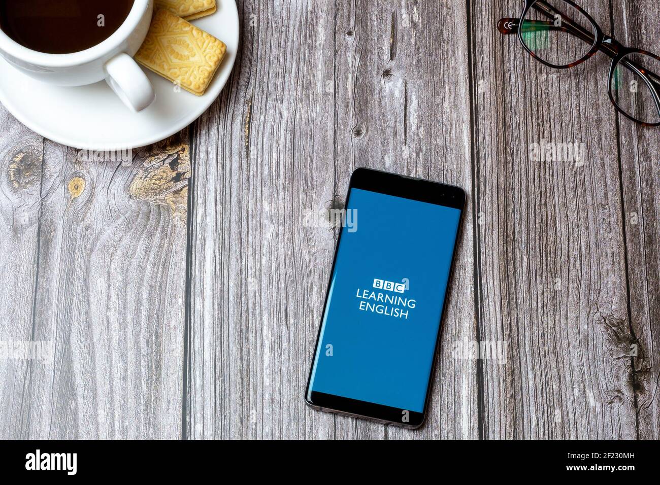 Un téléphone portable ou un téléphone portable sur une table en bois Avec l'application BBC Learning English ouverte à côté d'un café Banque D'Images