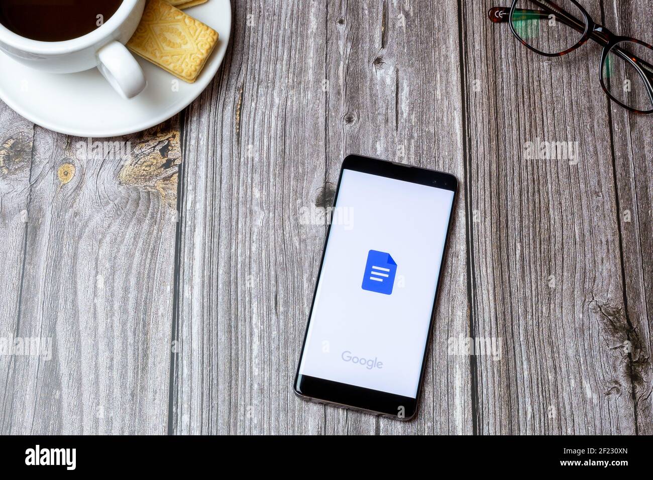 Un téléphone portable ou un téléphone portable sur une table en bois Avec l'application Google Docs ouverte à côté d'un café et lunettes Banque D'Images