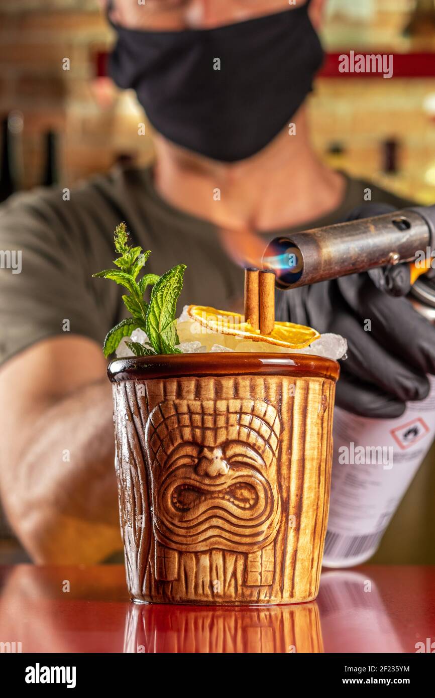 Le Barman met le feu à la cannelle dans un cocktail tiki au bar. Arrière-plan de la fête d'été. Banque D'Images