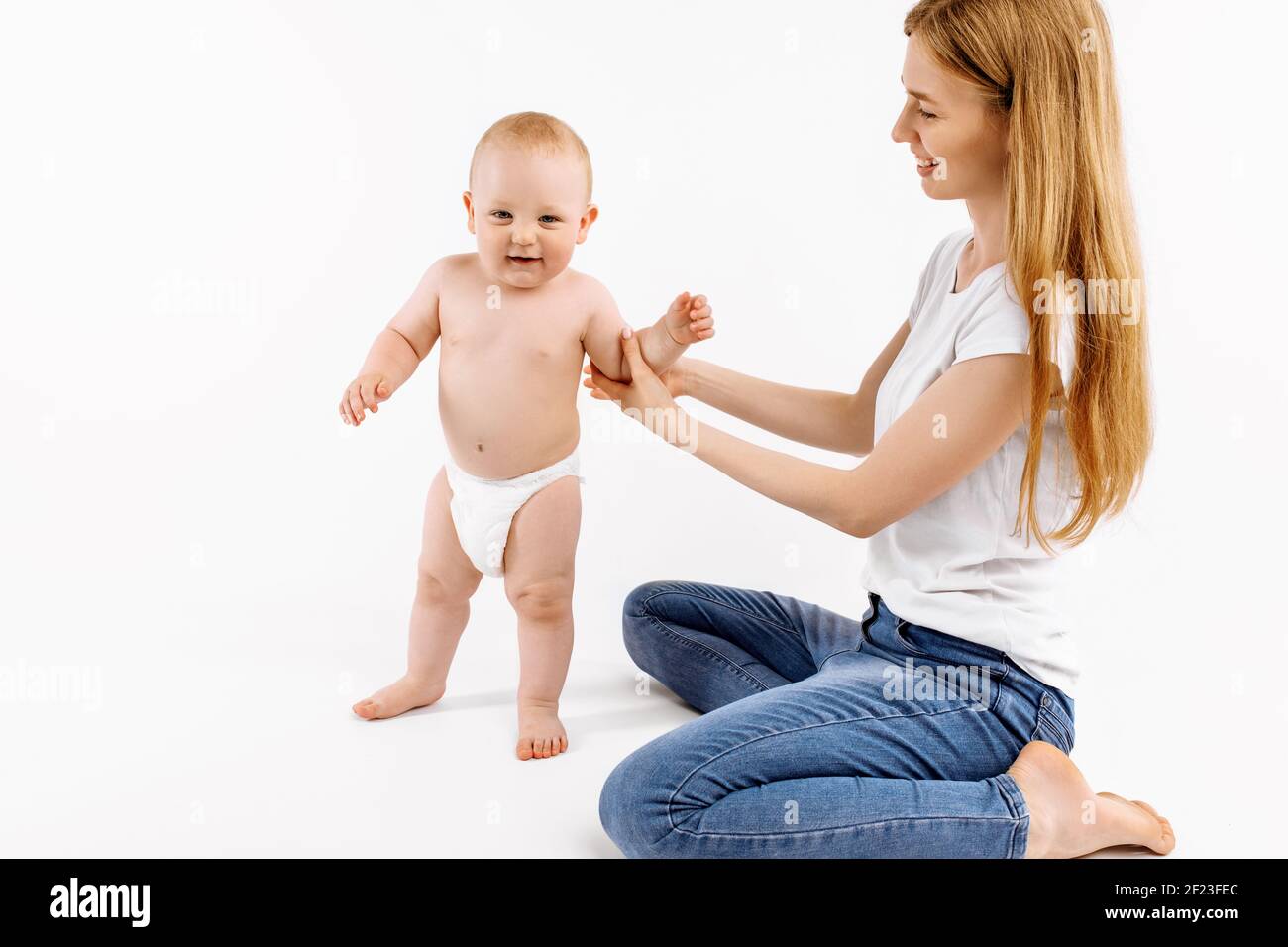 Petit enfant prenant les premiers pas, heureux petit enfant apprenant à marcher avec l'aide de la mère, sur un fond blanc, le concept de la croissance Banque D'Images