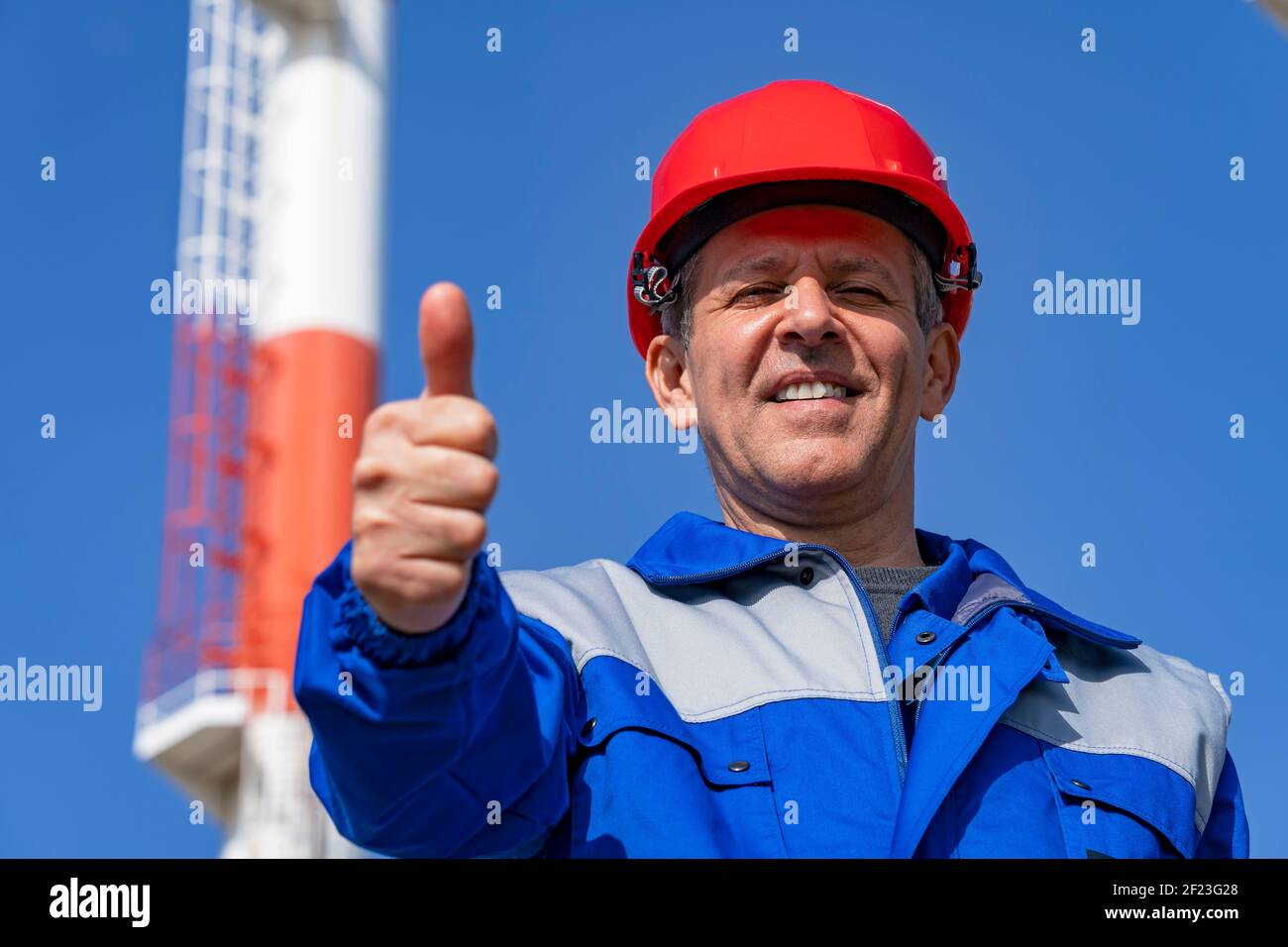 Un travailleur de la centrale électrique qui se donne contre les cheminées industrielles et le fond Blue Sky. Travailleur dans un équipement de protection individuelle regardant la caméra. Banque D'Images