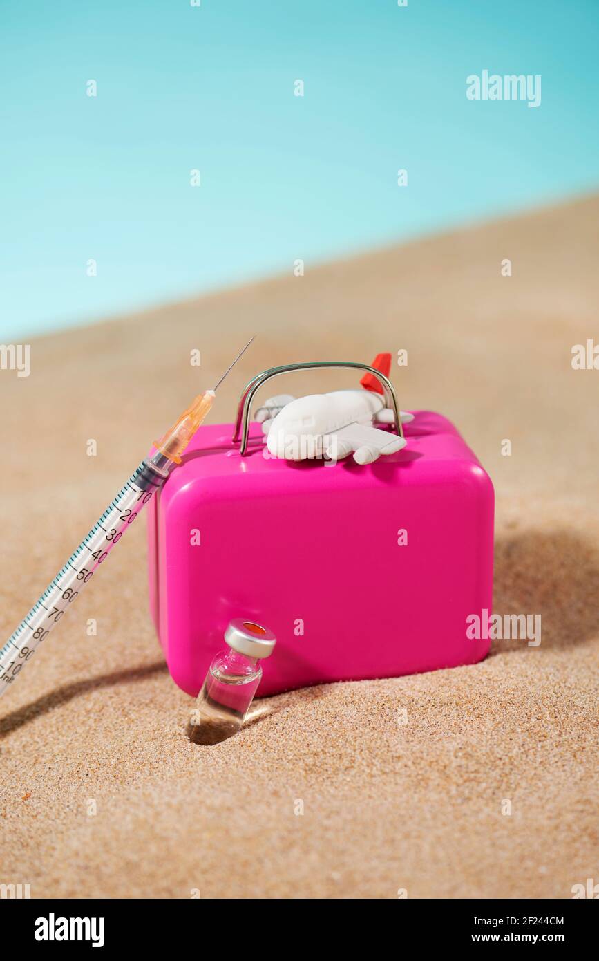 une seringue, un flacon, un avion et une valise rose sur le sable, sur fond bleu, représentant le tourisme médical Banque D'Images