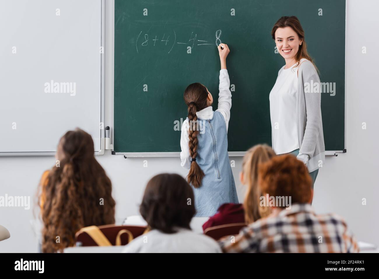 Vue Arrière Dune écolière écrivant Sur Un Tableau De Surveillance Près Dun Professeur Souriant