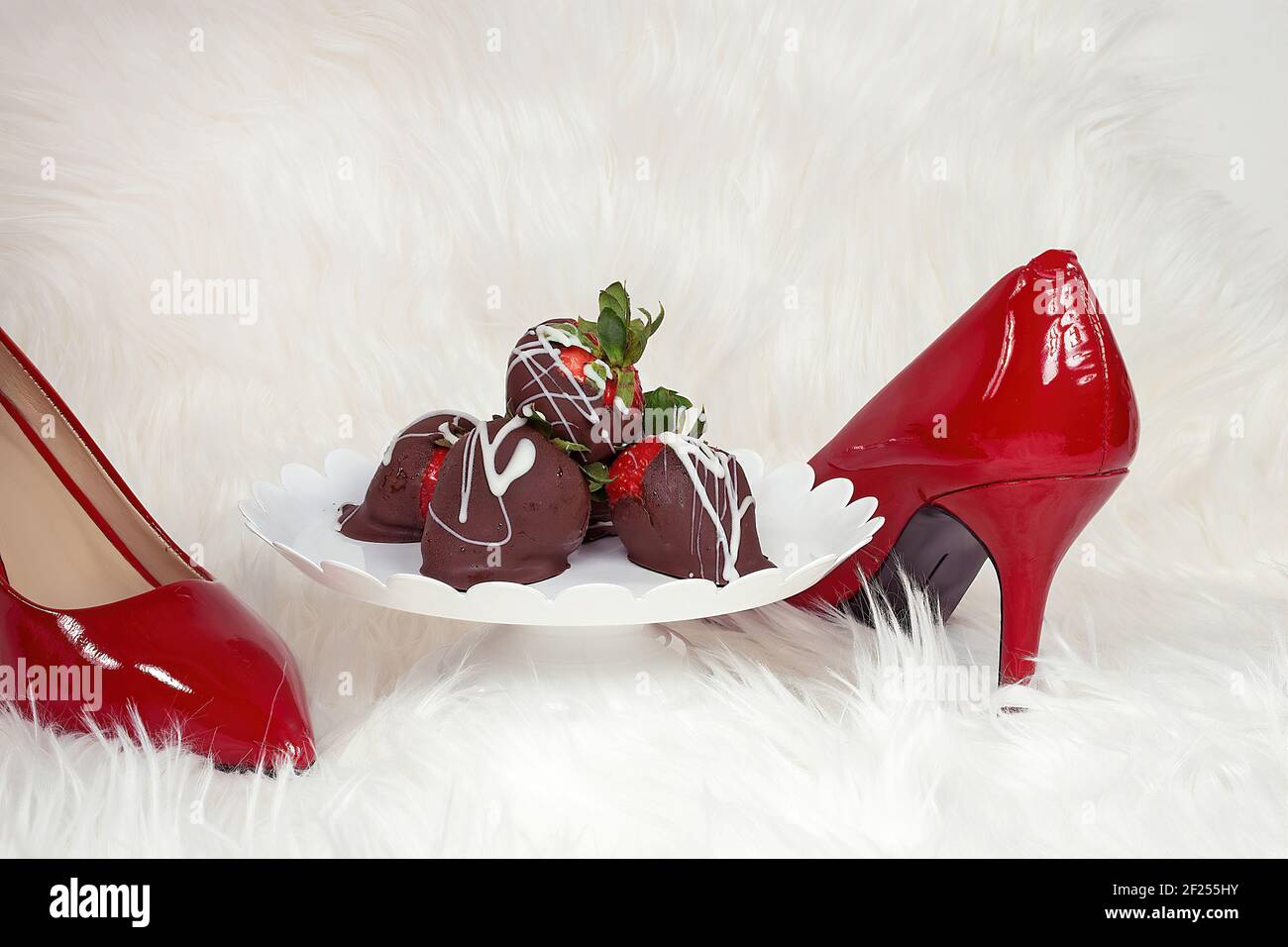 Fraises enrobées de chocolat sur un plat sur socle en fourrure blanche avec pompes rouges Banque D'Images
