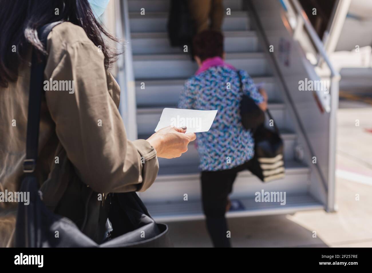 Femme voyageur dans un masque médical tenant une carte d'embarquement se trouvant dans l'avion. Banque D'Images